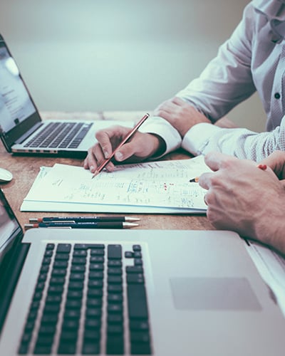 Two people working on a laptop and writing on a paper with pencil.  