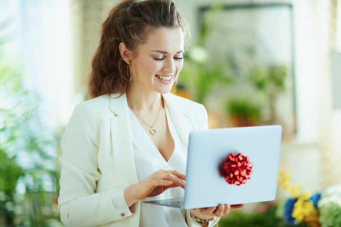 Woman smiling and holding a laptop with a red bow