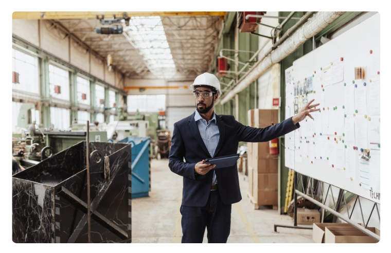 Man in hardhat standing in front of white board with data on it. Man in hardhat standing in front of white board with data on it.